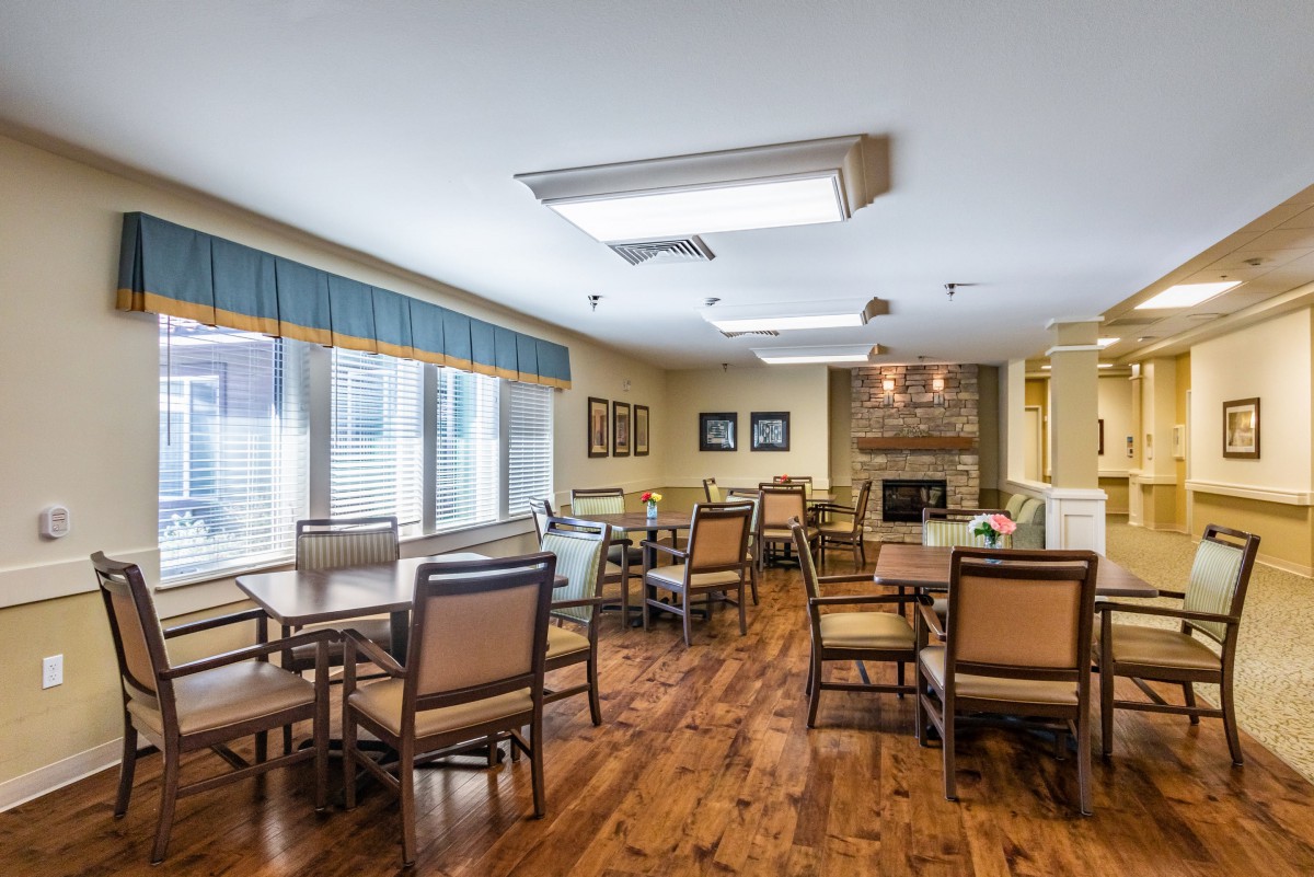 A cozy dining room with multiple tables and chairs, featuring a wooden floor and large windows.