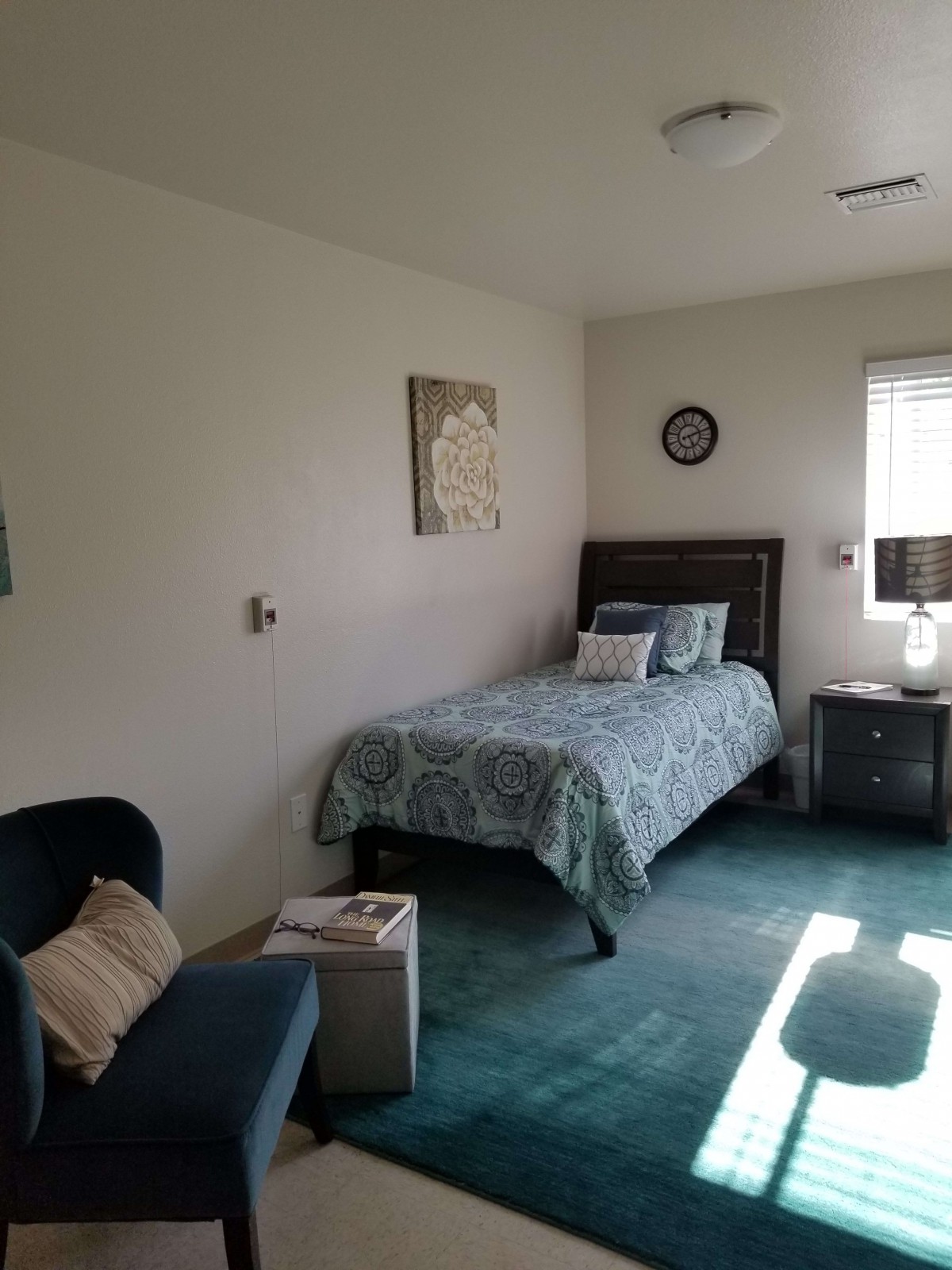 A cozy bedroom with a single bed, nightstand, and chair next to a window.