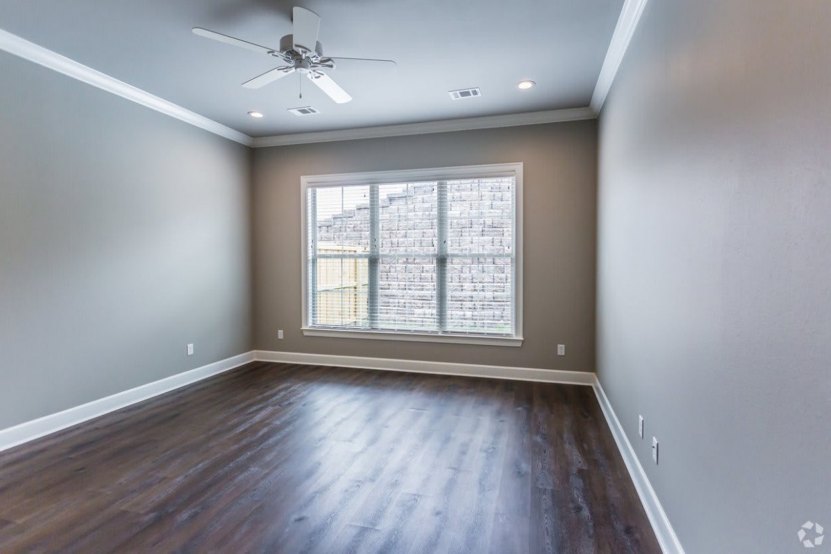 A bright, empty room with hardwood floors, a ceiling fan, and a large window.