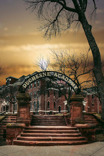 The iconic entrance of Duquesne Academy, framed by barren trees under a dramatic sunset.