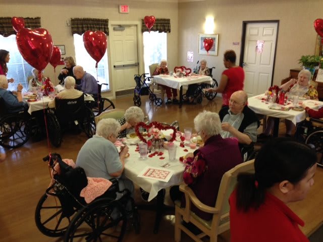 Elderly residents celebrating Valentine's Day in a nursing home with festive decorations and heart-shaped balloons.