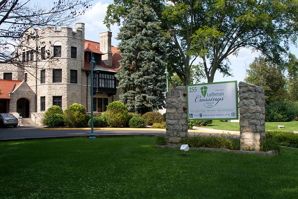A historic castle-like building with a well-maintained garden and a sign in the foreground.