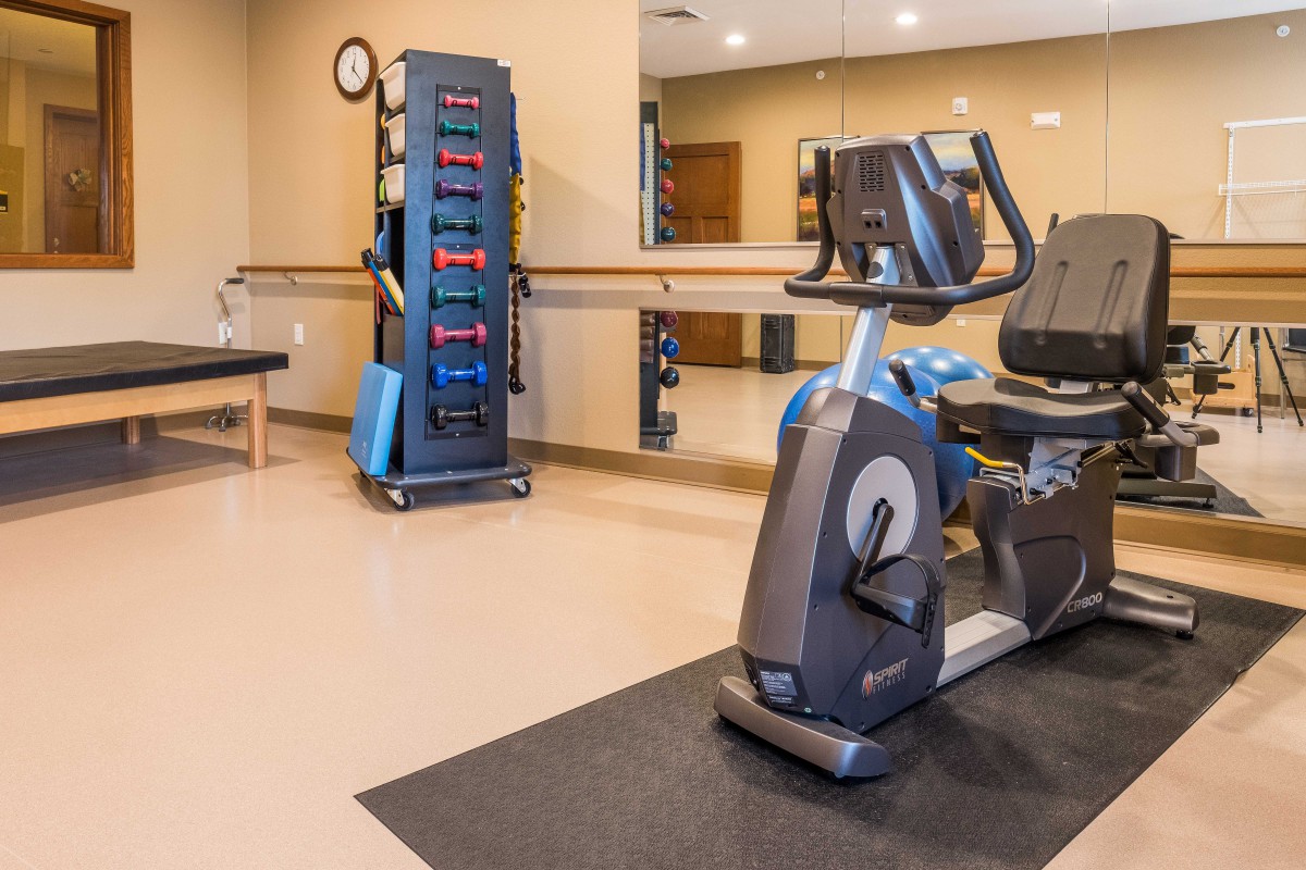 A small gym with an elliptical machine and a rack of colorful dumbbells.