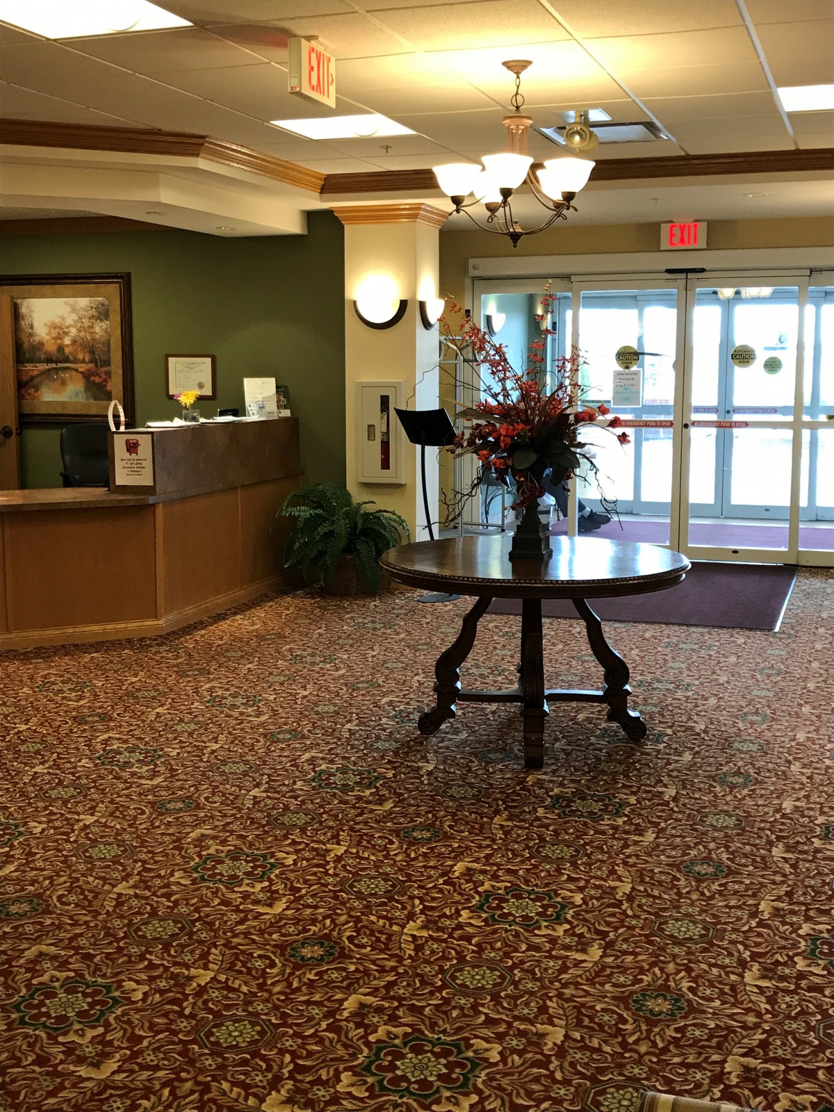 A hotel lobby with a reception desk, floral centerpiece, and entrance doors.