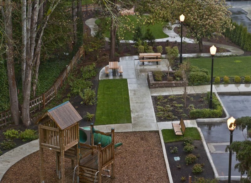 A scenic view of a park with a playground, benches, and lush greenery.