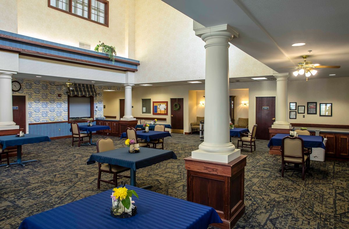 A well-lit dining area with blue tablecloths, surrounded by columns and decorated with flowers.