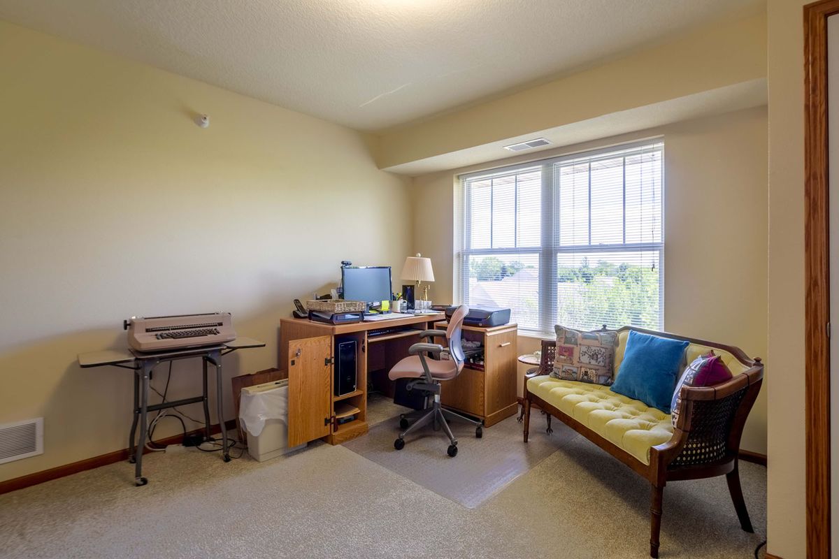 A cozy home office with a desk, computer, and sofa by a large window.