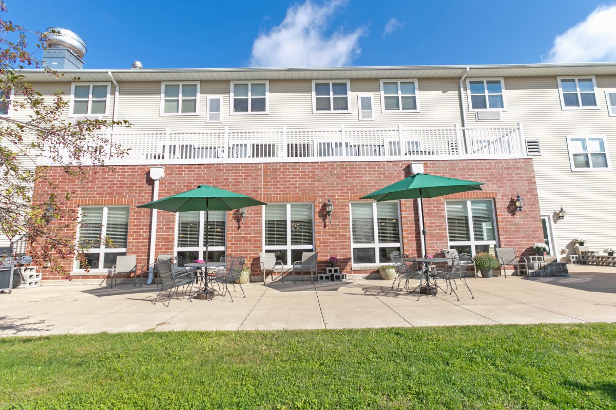 A building with a brick facade features outdoor seating with green umbrellas on a patio.