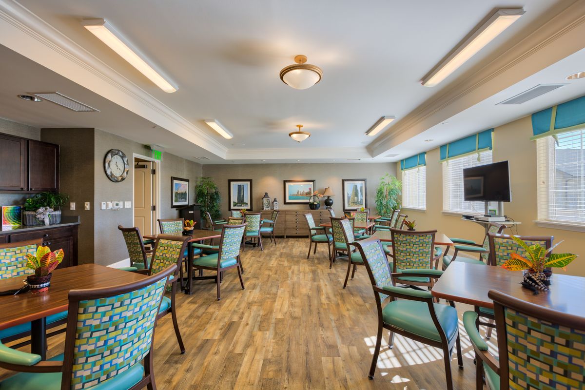 A well-lit dining area with multiple tables and chairs, featuring wooden flooring and decorative elements on the walls.