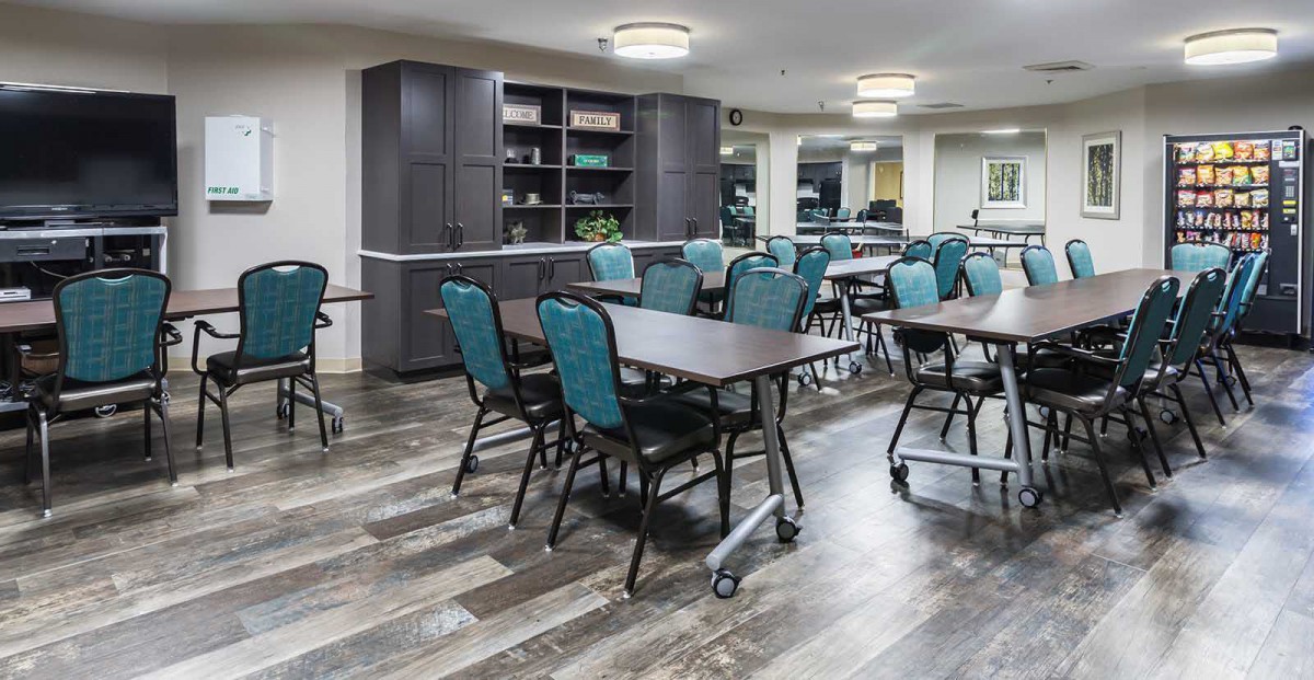 A spacious and well-lit dining or meeting area with multiple tables and chairs arranged, featuring modern interior design.