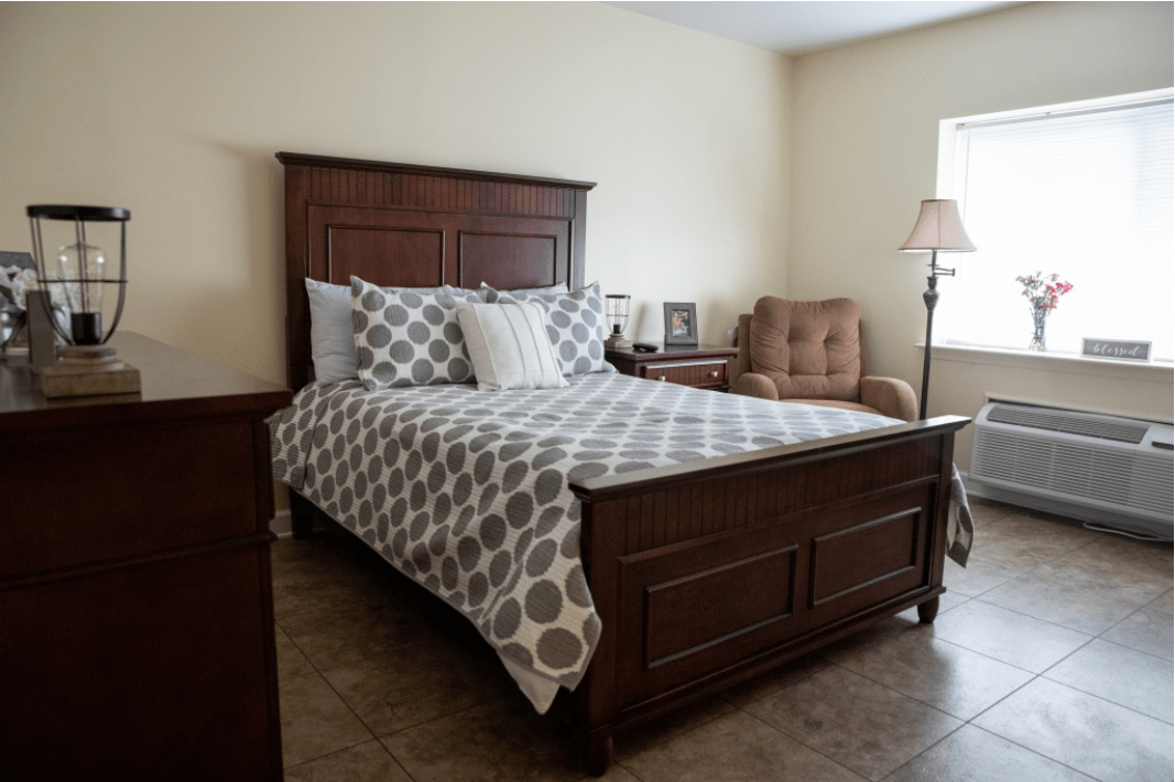 A cozy bedroom with a wooden bed, patterned bedding, and an armchair by the window.