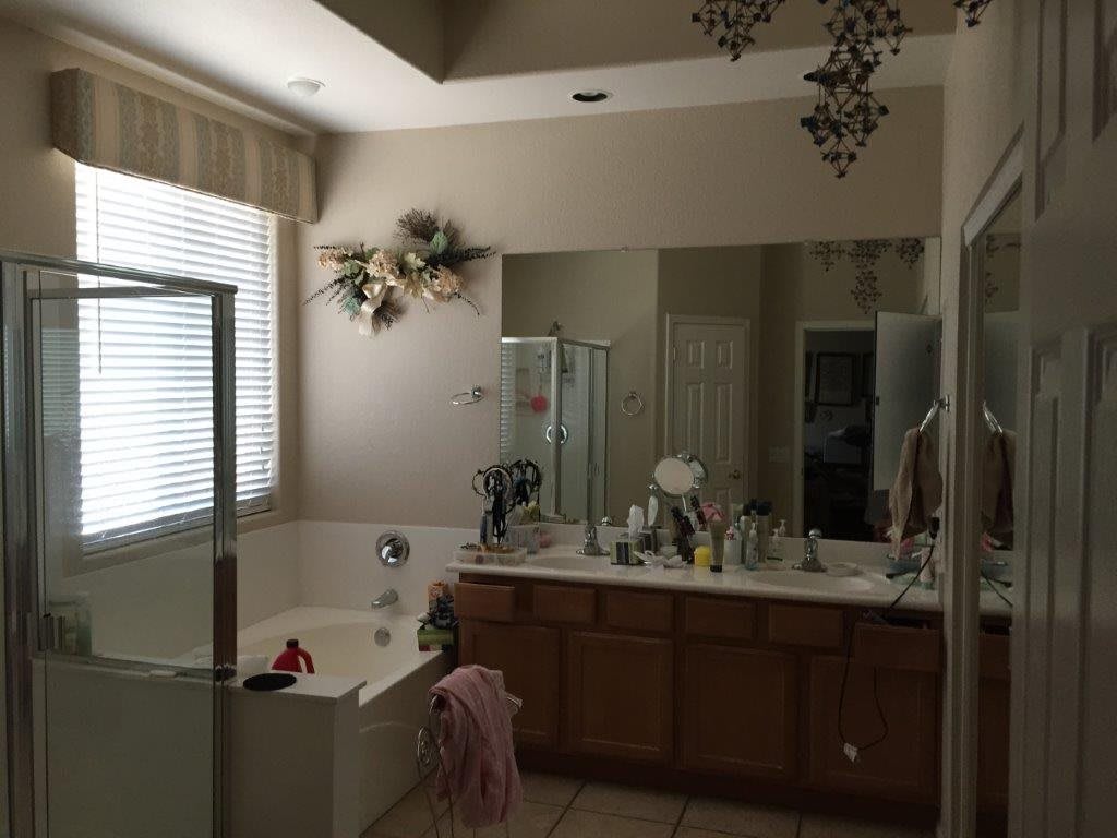 A spacious bathroom with a large mirror, bathtub, and sink, illuminated by natural light from a window.