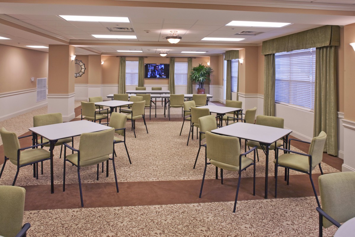 A spacious community dining room with several tables and chairs, featuring a television and large windows.