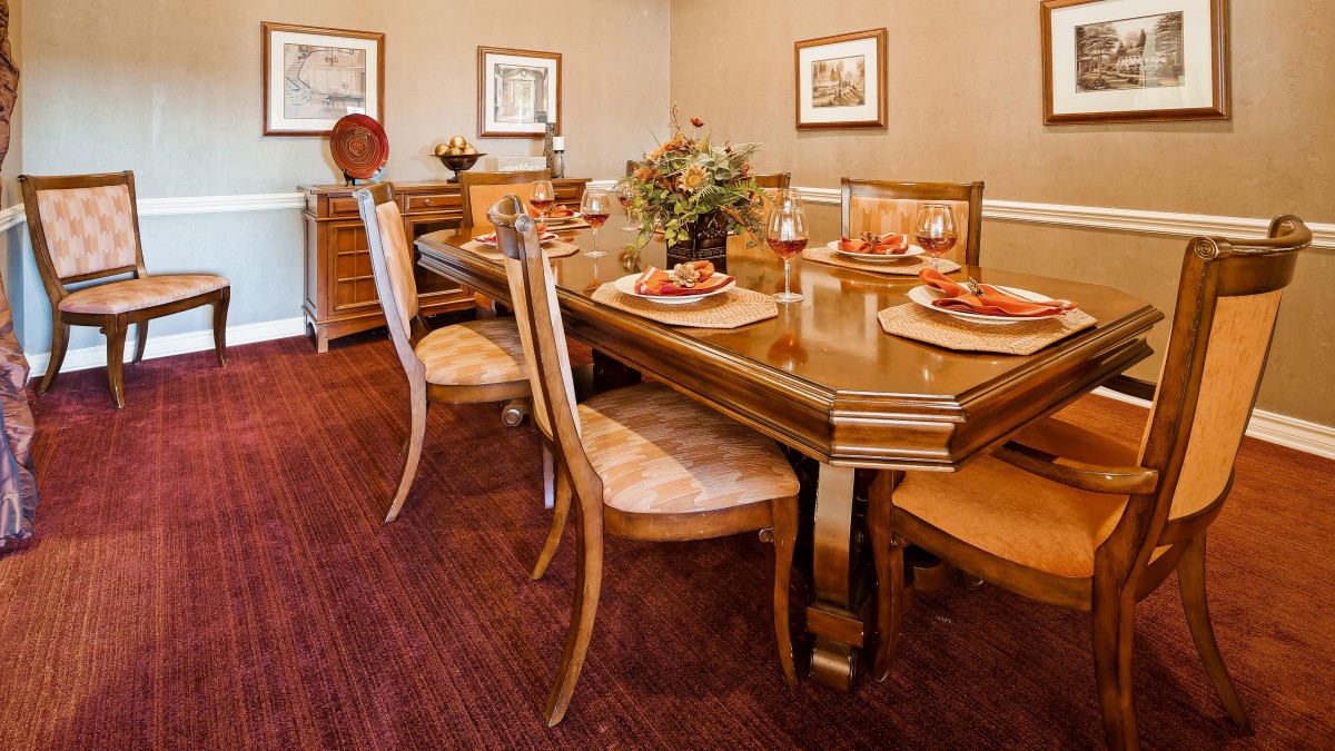 A formal dining room with a polished wooden table set for a meal, surrounded by matching chairs and classic decor.