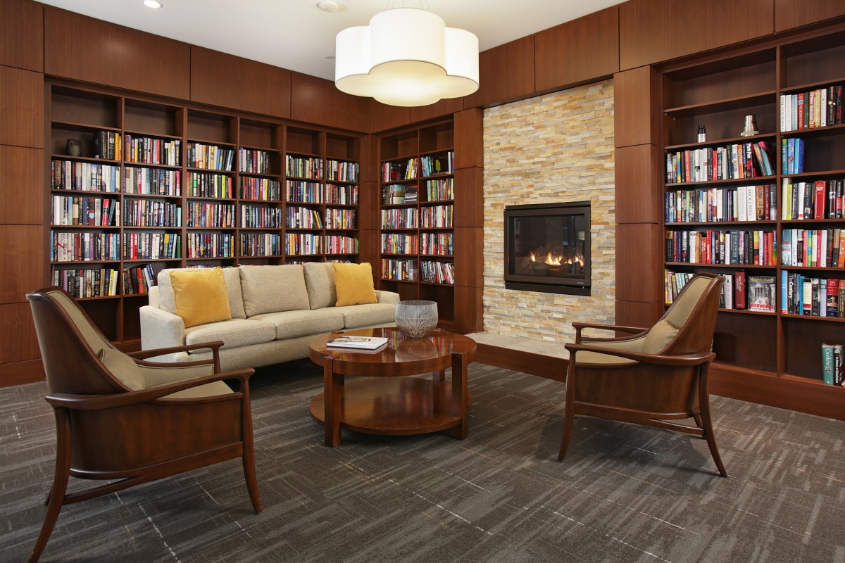 A cozy library space with a sofa, armchairs, and a fireplace surrounded by bookshelves.