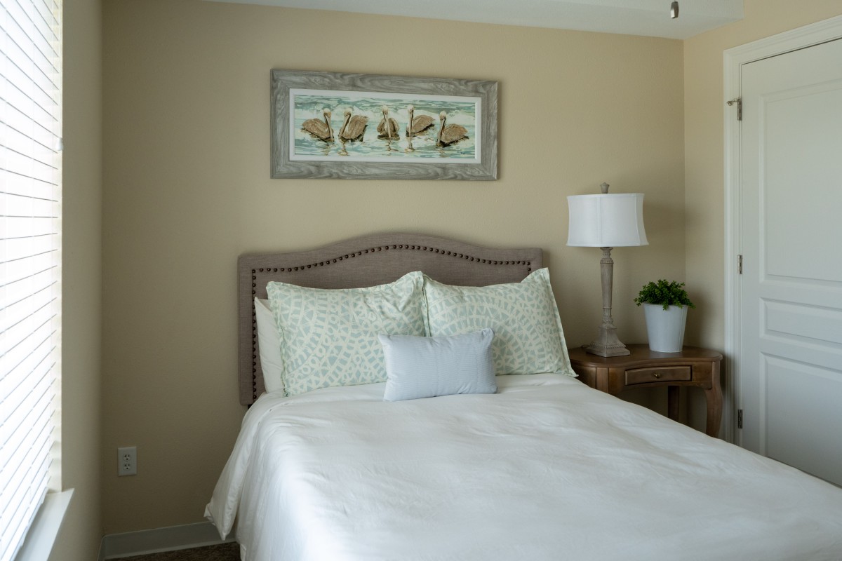A cozy bedroom with a neatly made bed, decorative pillows, and a framed picture above the headboard.
