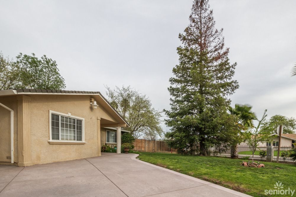 A suburban house with a spacious driveway and a well-maintained yard featuring tall trees.