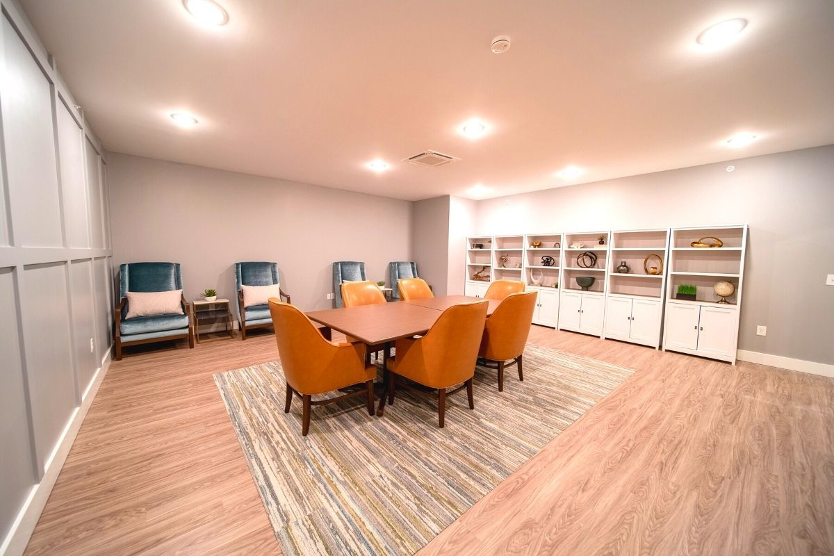 A modern conference room featuring a wooden table surrounded by orange chairs, with library shelves in the background.