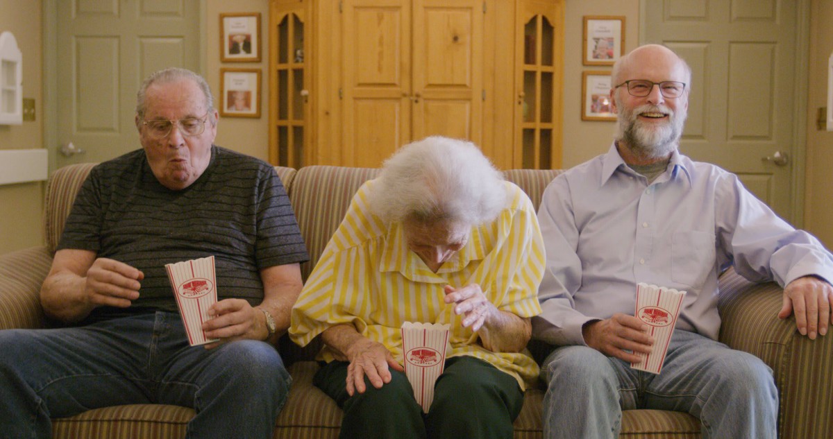 Three elderly people sitting on a couch enjoying popcorn together.