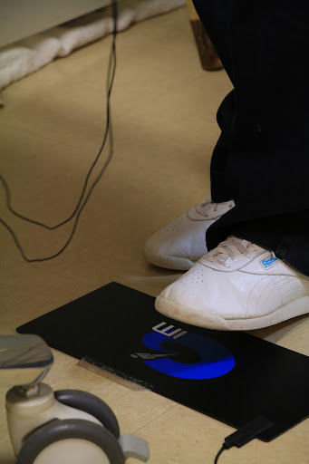 A person's foot wearing a white shoe is positioned on a device that emits blue light.