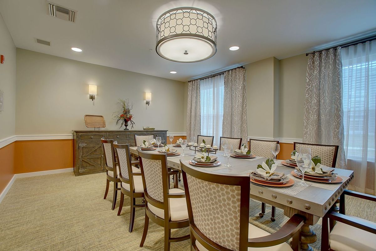 Elegant dining room with a long table set for a meal, featuring upholstered chairs and a decorative chandelier.