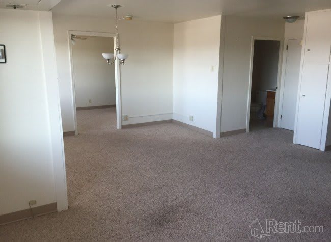A spacious and empty living area with neutral-colored walls and a carpeted floor.