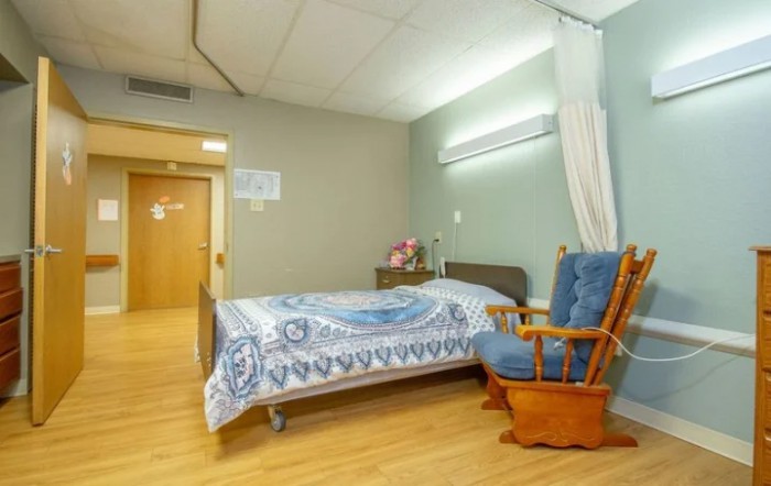 A tidy hospital room featuring a bed and a rocking chair.