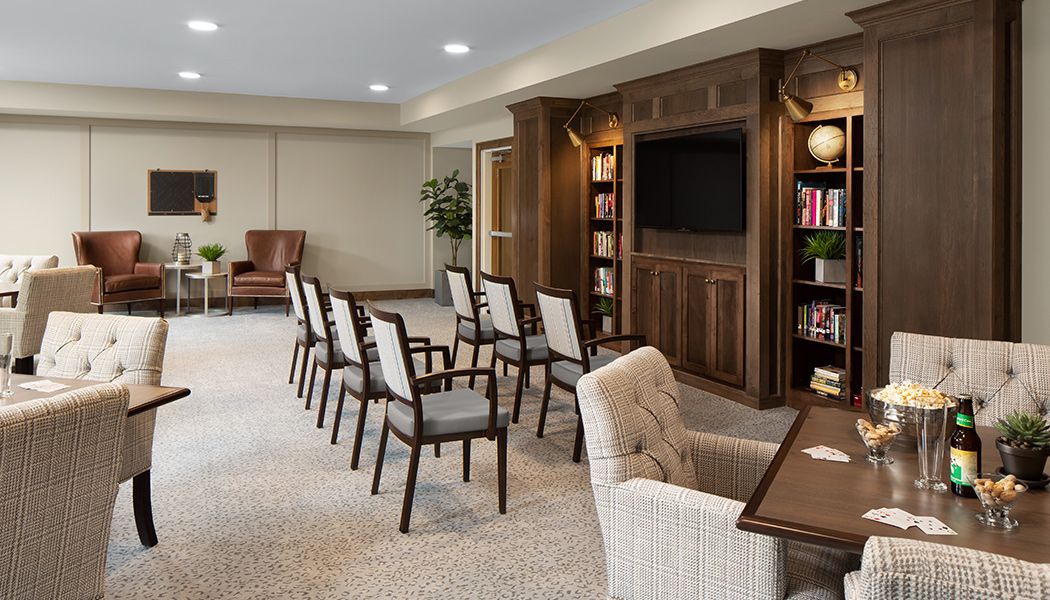 A cozy meeting room with chairs arranged in rows, a large bookshelf, and a television mounted on the wall.