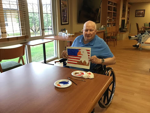 An elderly man proudly showcases his painting of the American flag during an art activity.