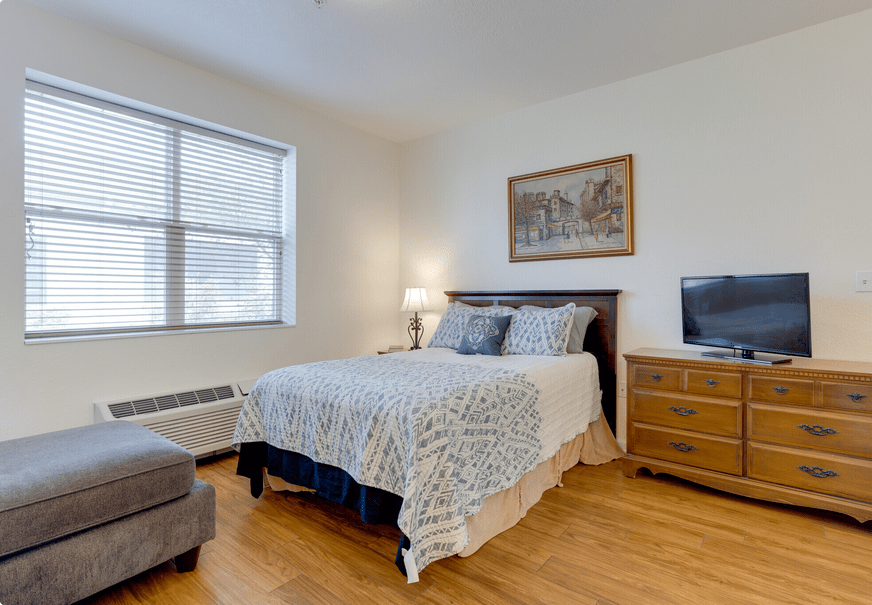 A well-lit bedroom with a cozy bed, artwork on the wall, and a television.