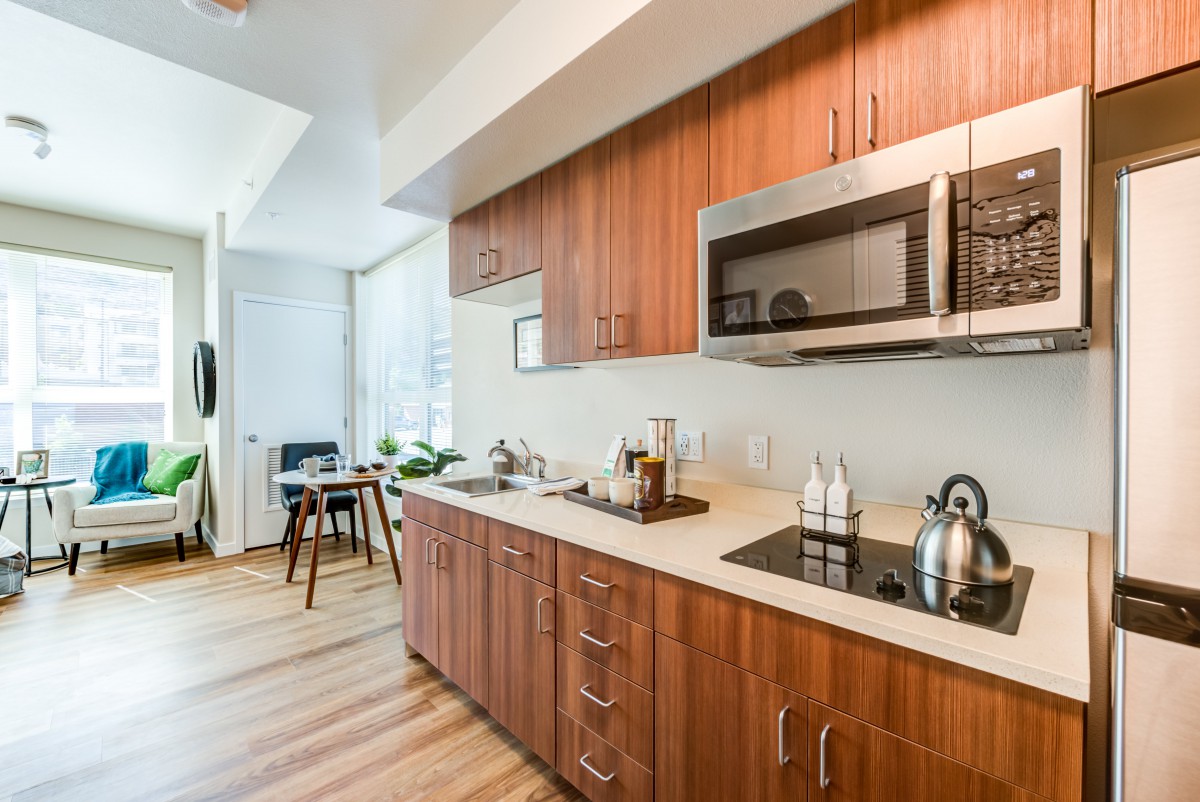 A modern kitchen with wooden cabinets, featuring a stovetop and microwave.
