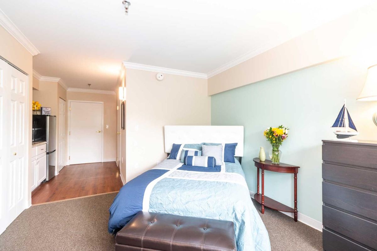 A modern bedroom with a neatly made bed, featuring blue and white bedding, flanked by a small table with flowers.