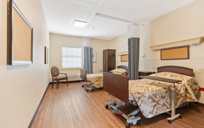 A clean and organized hospital room with two beds, separated by curtains and featuring wooden flooring.