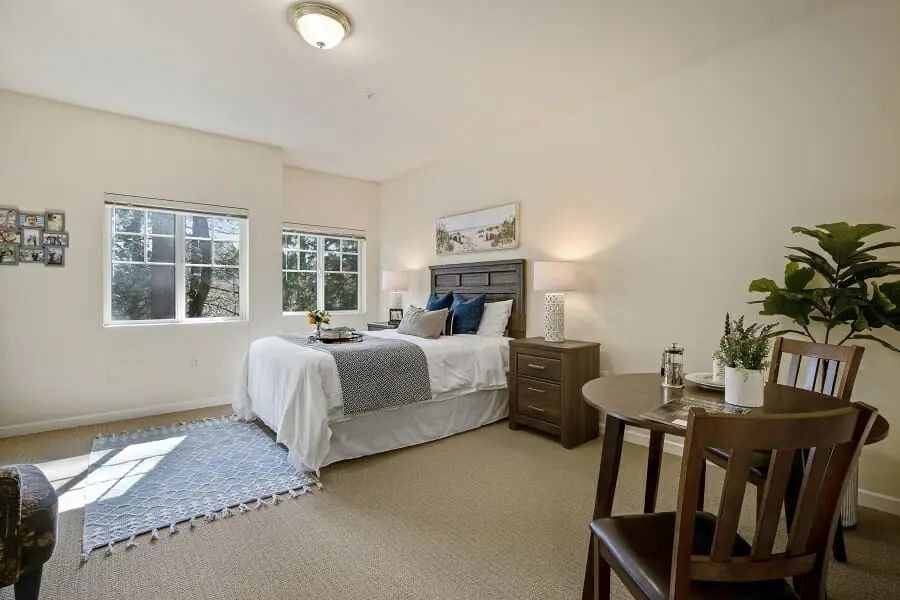 A cozy bedroom with a neatly made bed, side tables, and natural light streaming through the windows.