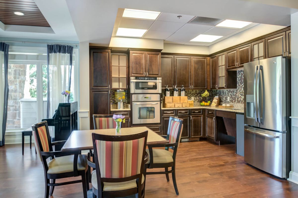 A modern kitchen and dining area featuring wood cabinets, contemporary appliances, and a small dining table with chairs.