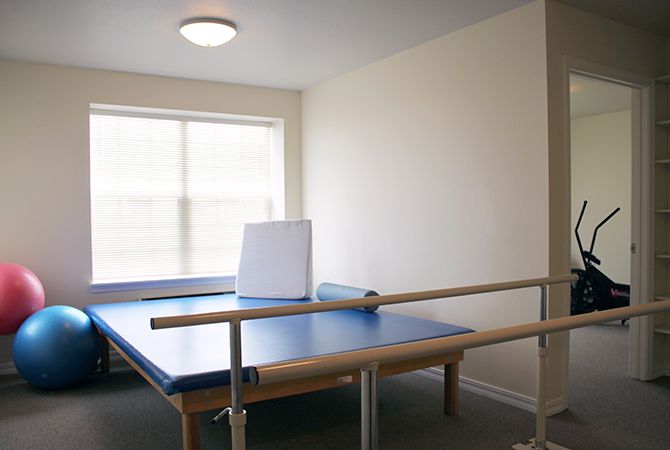 A clean and well-lit physical therapy room featuring parallel bars and a mat table.