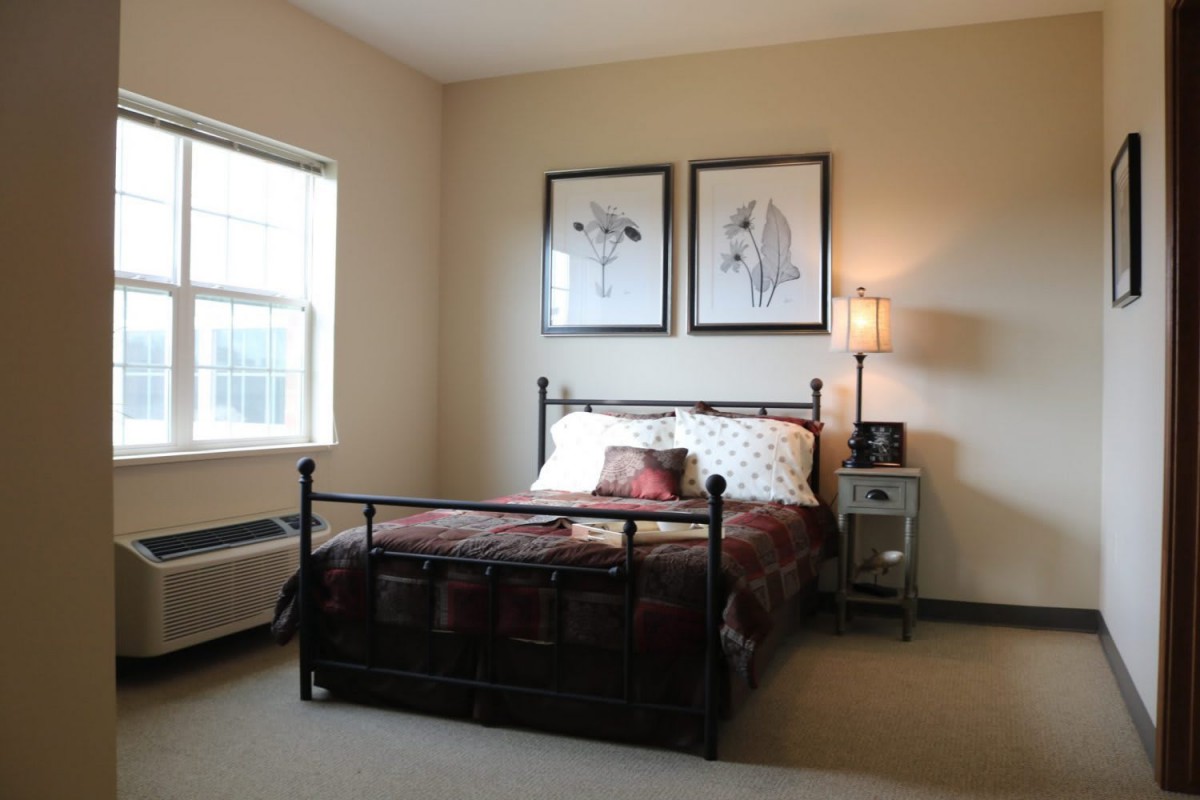 A cozy bedroom featuring a metal-frame bed with patterned bedding, wall art, and a bedside table with a lamp.