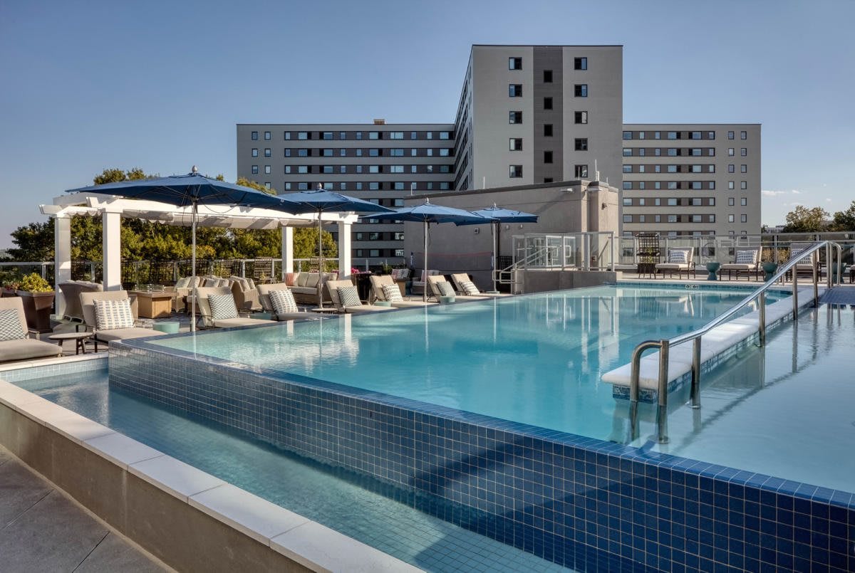 A rooftop swimming pool with sun loungers overlooking an urban hotel.