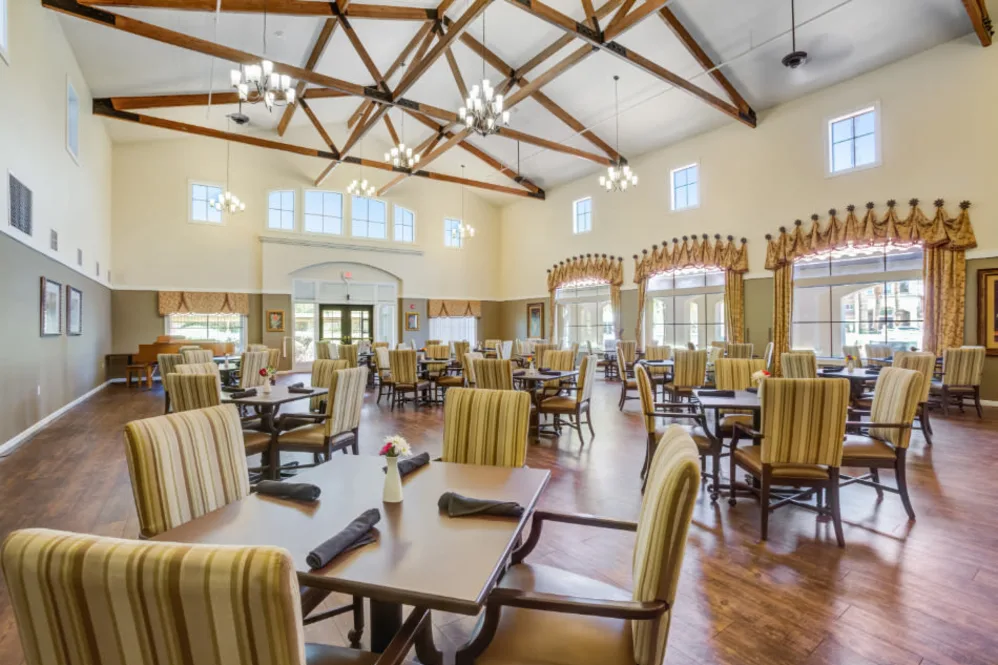 A spacious dining room with high ceilings, featuring multiple tables and striped chairs.