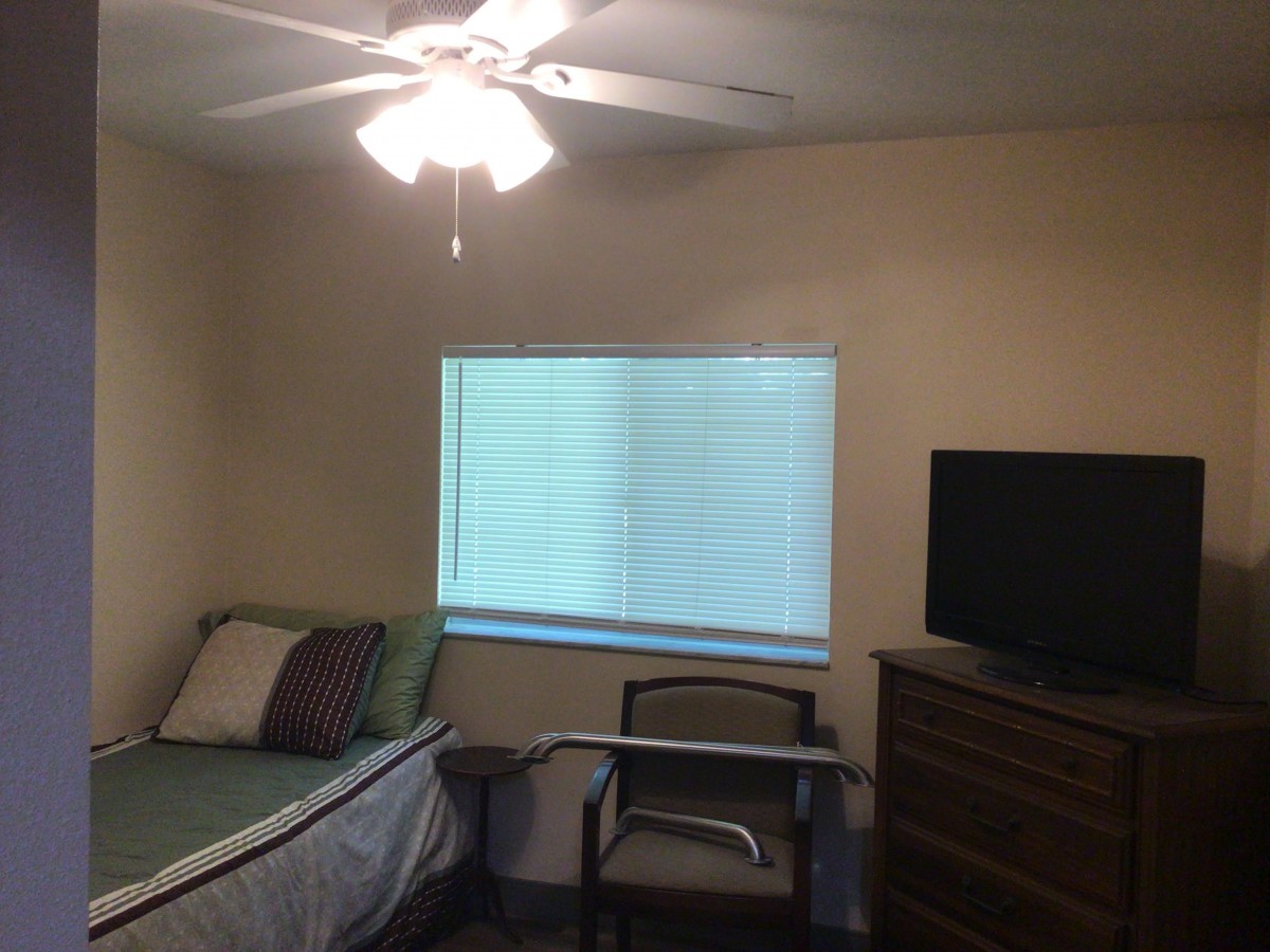 A small bedroom with a single bed, ceiling fan, and TV.