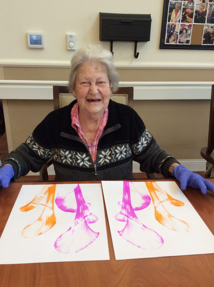 An elderly woman smiling while showcasing her abstract artwork.