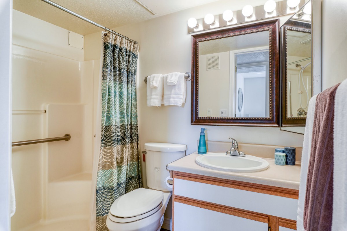 A well-lit bathroom with a sink, mirror, toilet, and a shower area with a curtain.