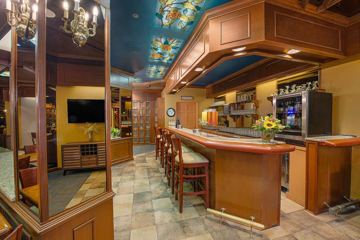 A cozy bar interior with wooden furnishings and a decorative ceiling.