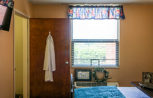 A cozy bedroom featuring a door, window with colorful curtains, and a neatly made bed.