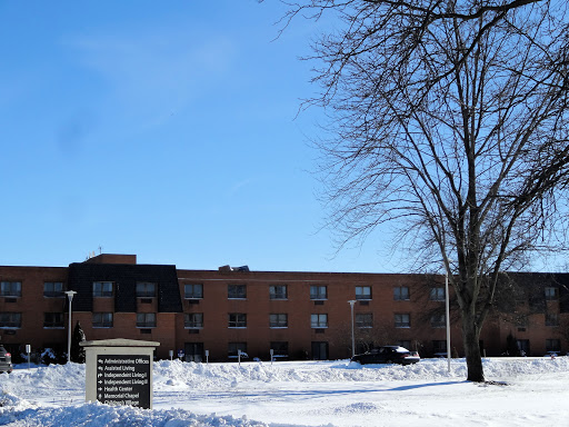 A winter scene featuring a brick building surrounded by snow and a bare tree under a clear blue sky.