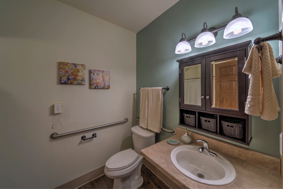 A well-lit bathroom with a toilet, sink, mirror, and decorative artwork on the walls.