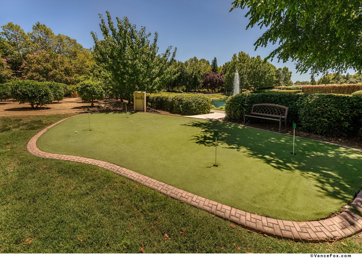A well-maintained outdoor putting green surrounded by lush landscaping and a bench.