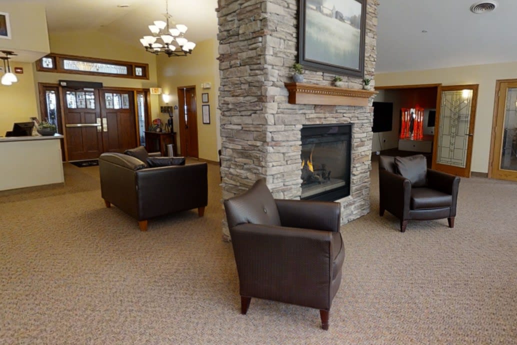 A cozy living room with a stone fireplace, leather chairs, and carpeted flooring.