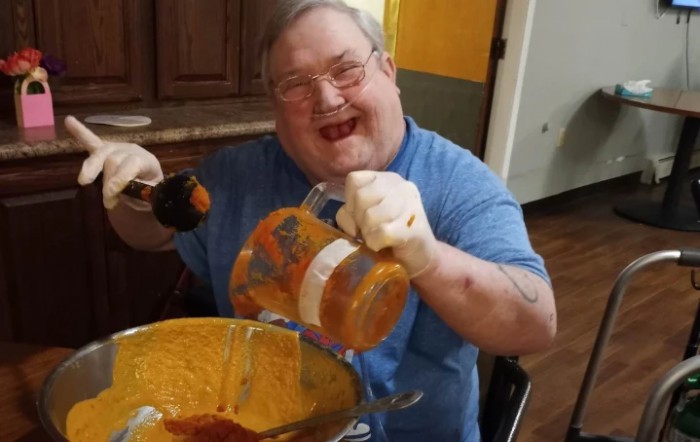 A person happily preparing food with a blender in the kitchen.