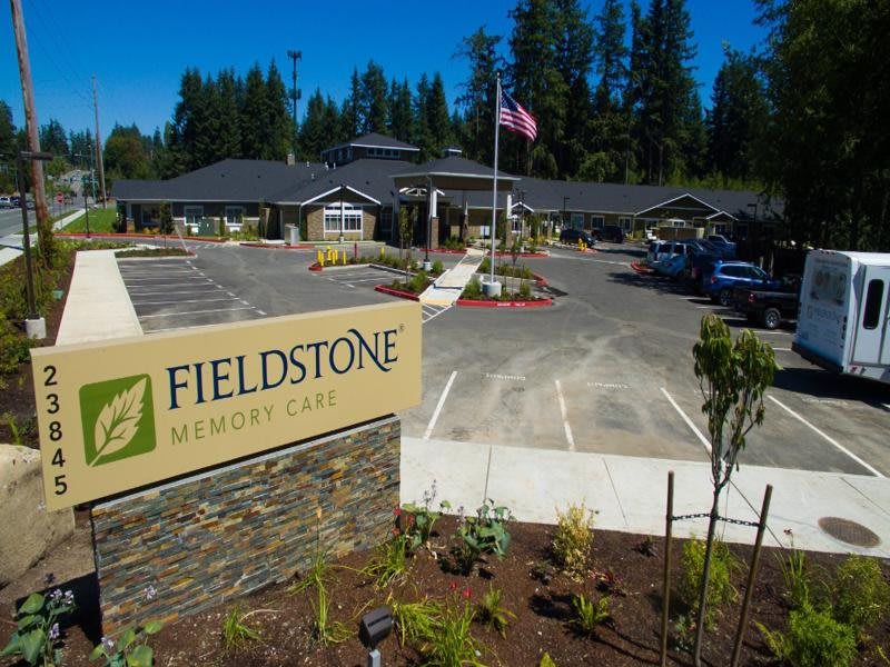 A view of the Fieldstone Memory Care facility, featuring a building with a landscaped entrance and parking area.